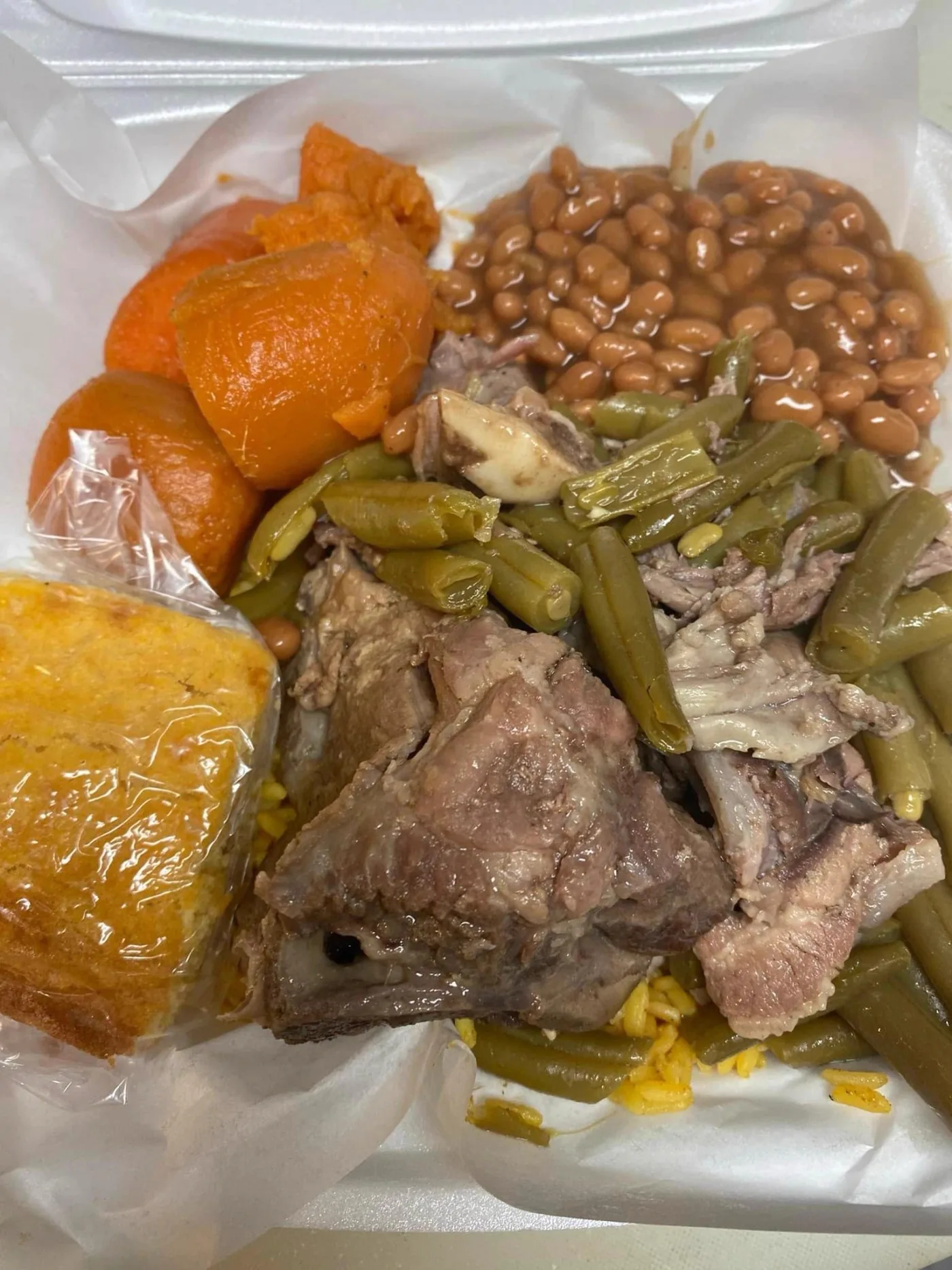 A Hot Girlz Soulfood plate: candied yams, baked beans, green beans with smoked meat, oxtail, cornbread and yellow rice.